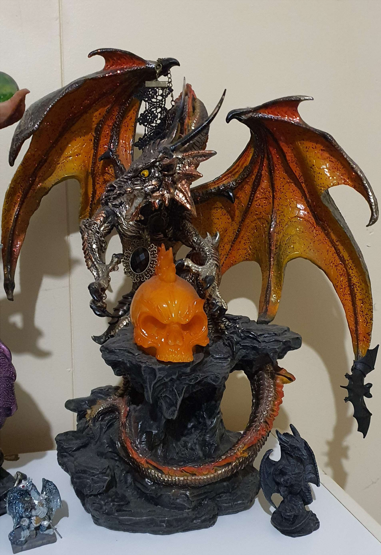 A large orange  dragon statue. It is perched upon a rocky ledge, and protects a large, orange human skull.