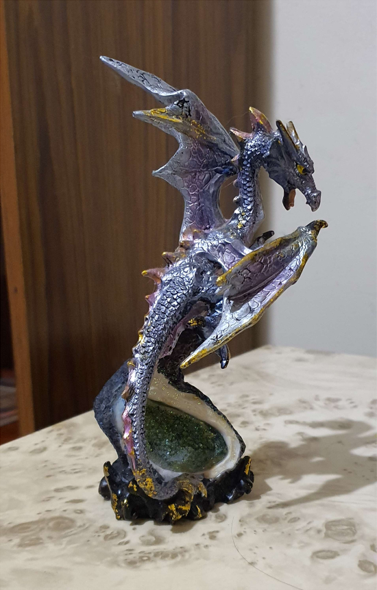A dragon statue that is lavender in colour. It is perched on top of a geode.