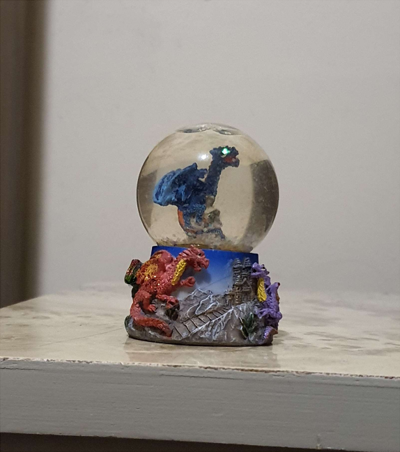 Small snowglobe with a blue dragon figure inside of it.